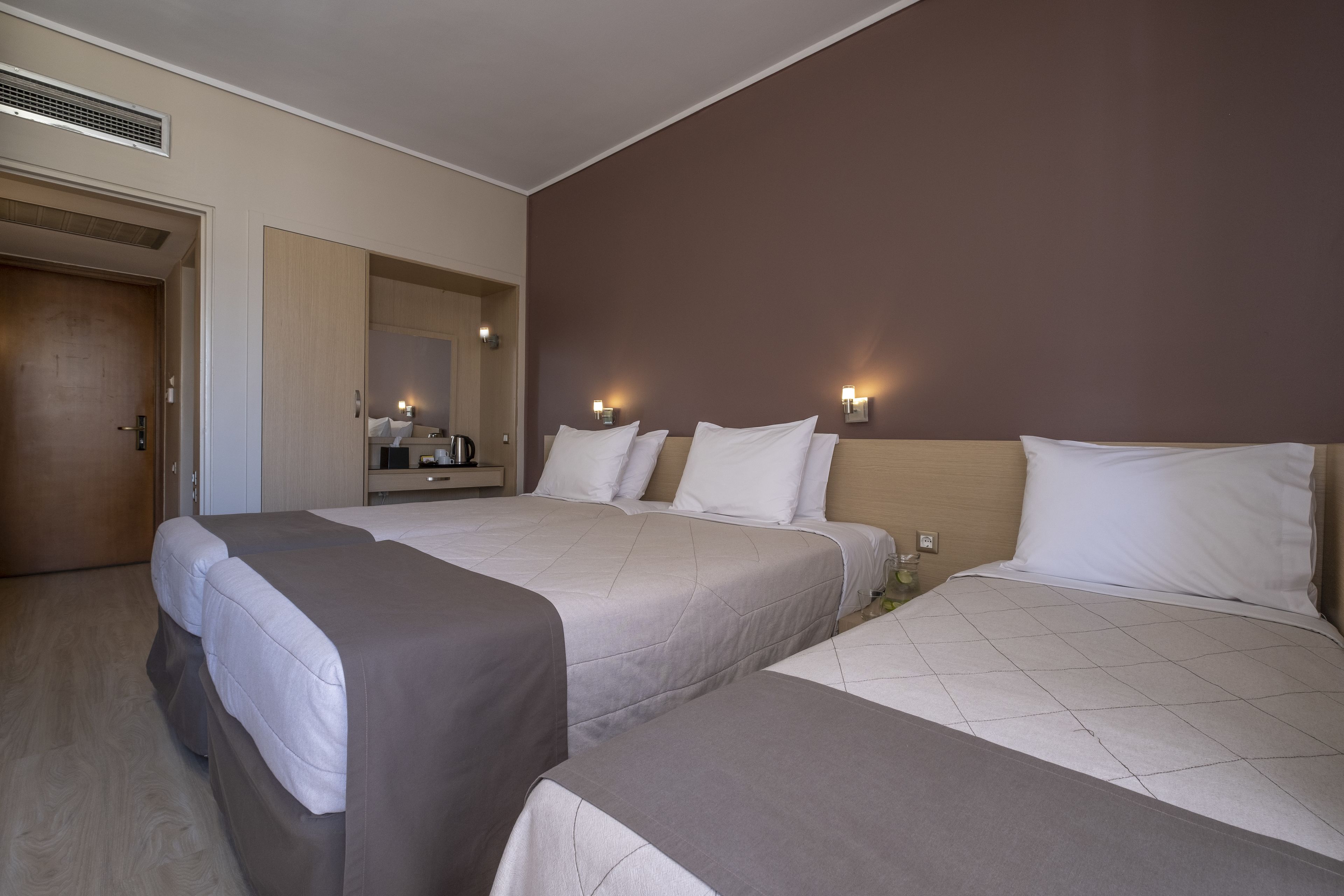 Ett hotellrum med två sängar, en trädörr, en spegel och väggmonterade lampor.