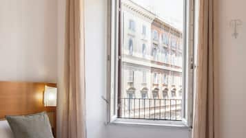 Habitación de hotel con dos camas, una ventana con cortinas, un radiador y vistas a edificios.