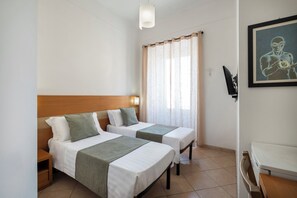 Ein Hotelzimmer mit zwei Einzelbetten, einem Holzkopfende, einem Fenster mit durchsichtigen Vorhängen, einem gerahmten Kunstwerk an der Wand und einem Flachbildfernseher.