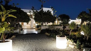 A well-lit outdoor area with a gravel path leading to a building with a white facade. There are various potted plants and trees around the area. - Hotel Ristorante Cavalluccio Marino (Lampedusa)
