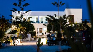A modern building with a white facade, a balcony, and a patio area with potted plants and a parked scooter. - Hotel Ristorante Cavalluccio Marino (Lampedusa)