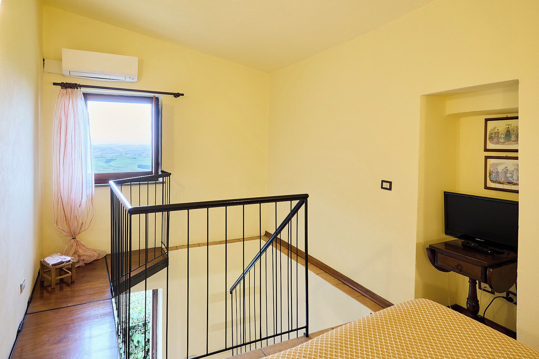 Una habitación con escalera de madera, ventana con vistas, televisor y una mesita.