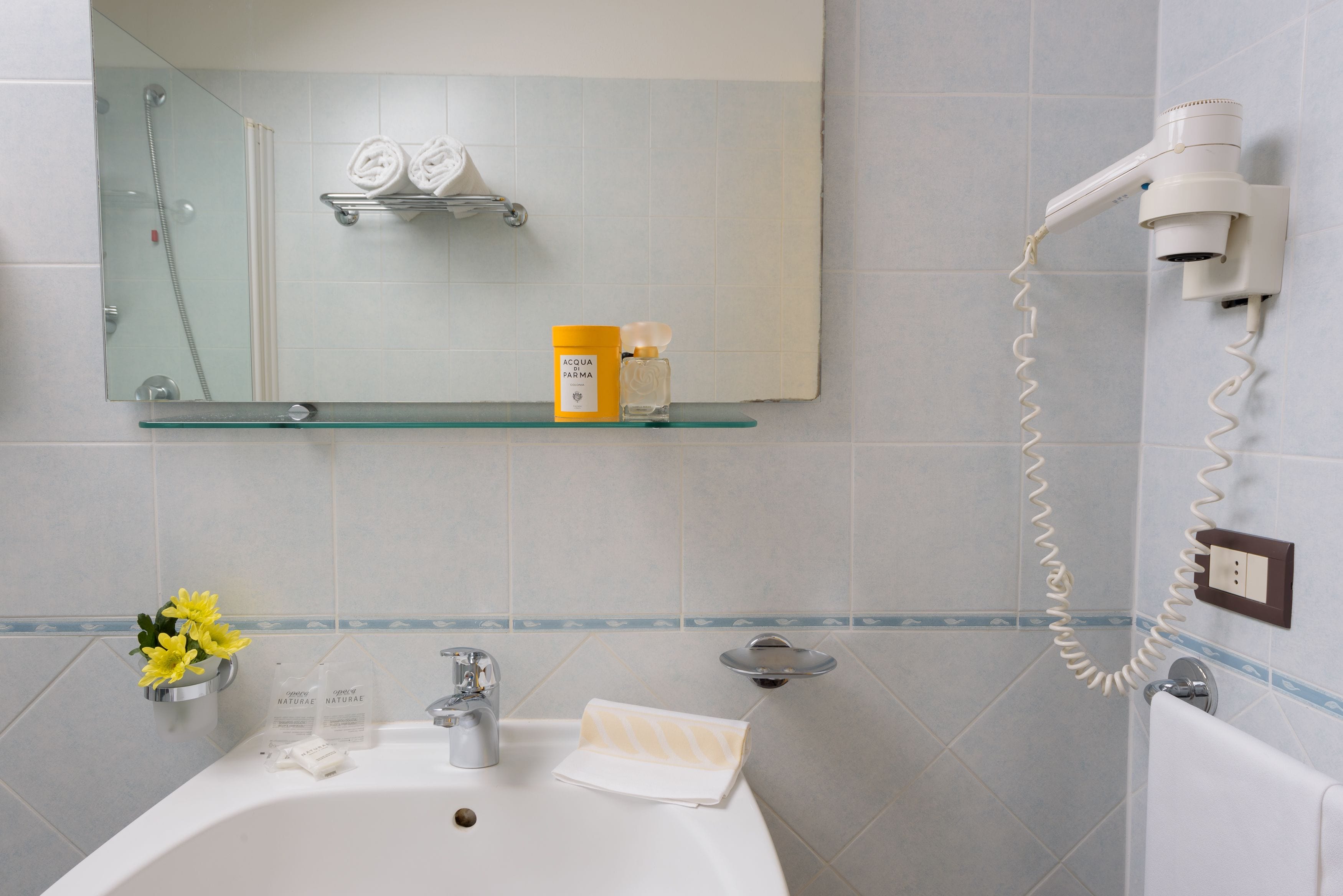 Ein Badezimmer mit einer Glasablage für Toilettenartikel, einem Spiegel über dem Waschbecken und einem an der Wand befestigten Fön.