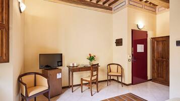A small, cozy room with a television, a desk with a vase of flowers, two chairs, and a red door.