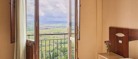 A bedroom with a large window offering a view of a green landscape.