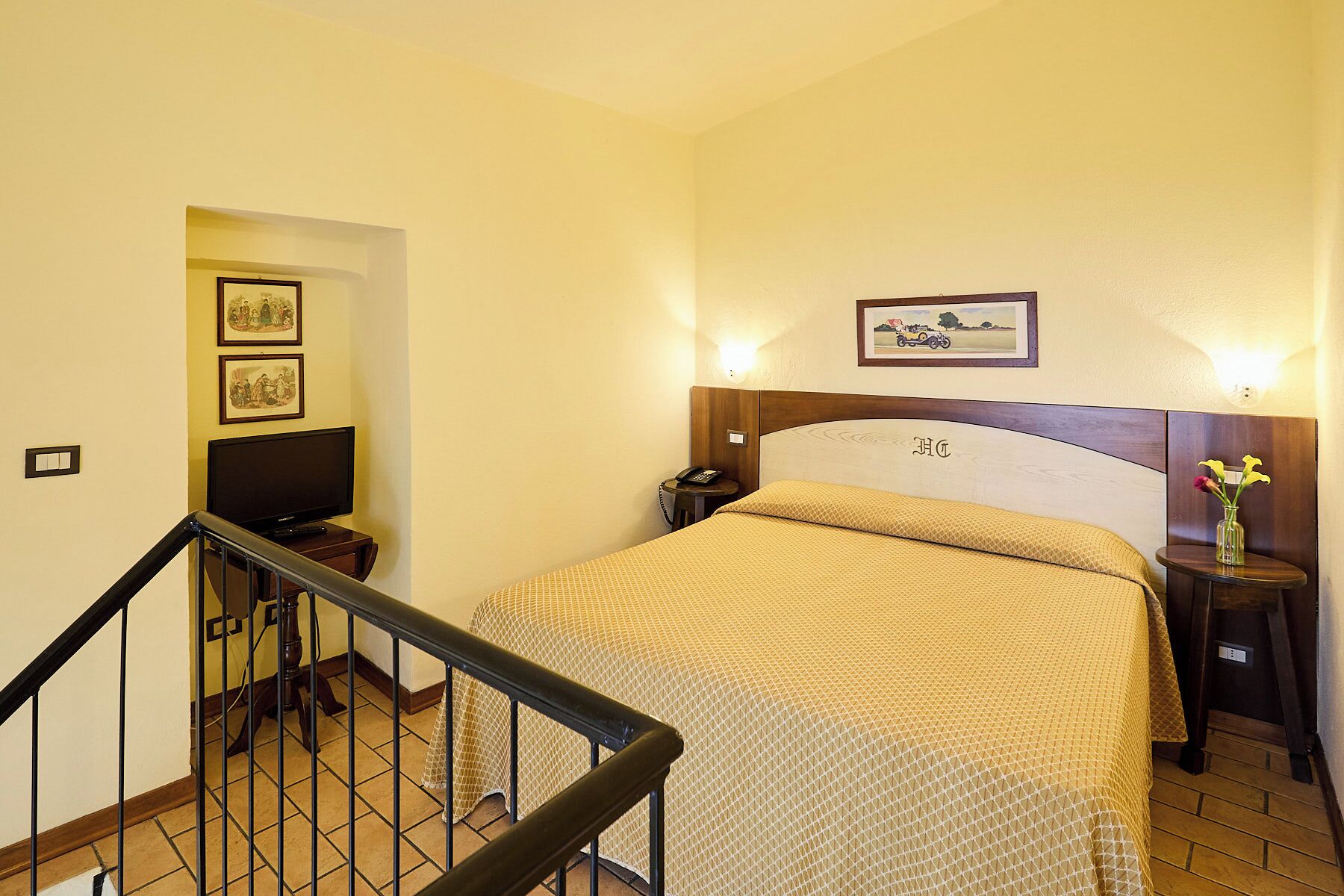 A hotel room with a bed, a TV, a nightstand with a phone, and a picture on the wall.