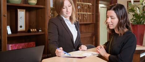 Two individuals at a wooden counter with a map, surrounded by shelves with various items.
