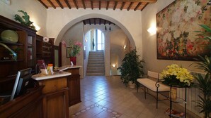 Un vestíbul ampli amb sòl de rajola, mostrador de recepció de fusta, una escala i un gran quadre floral a la paret.