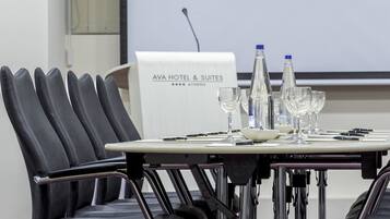 Une salle de conférence avec une table préparée pour une réunion, équipée de chaises, d’un écran de projection et d’une enseigne indiquant « AYA HOTEL & SUITES ».