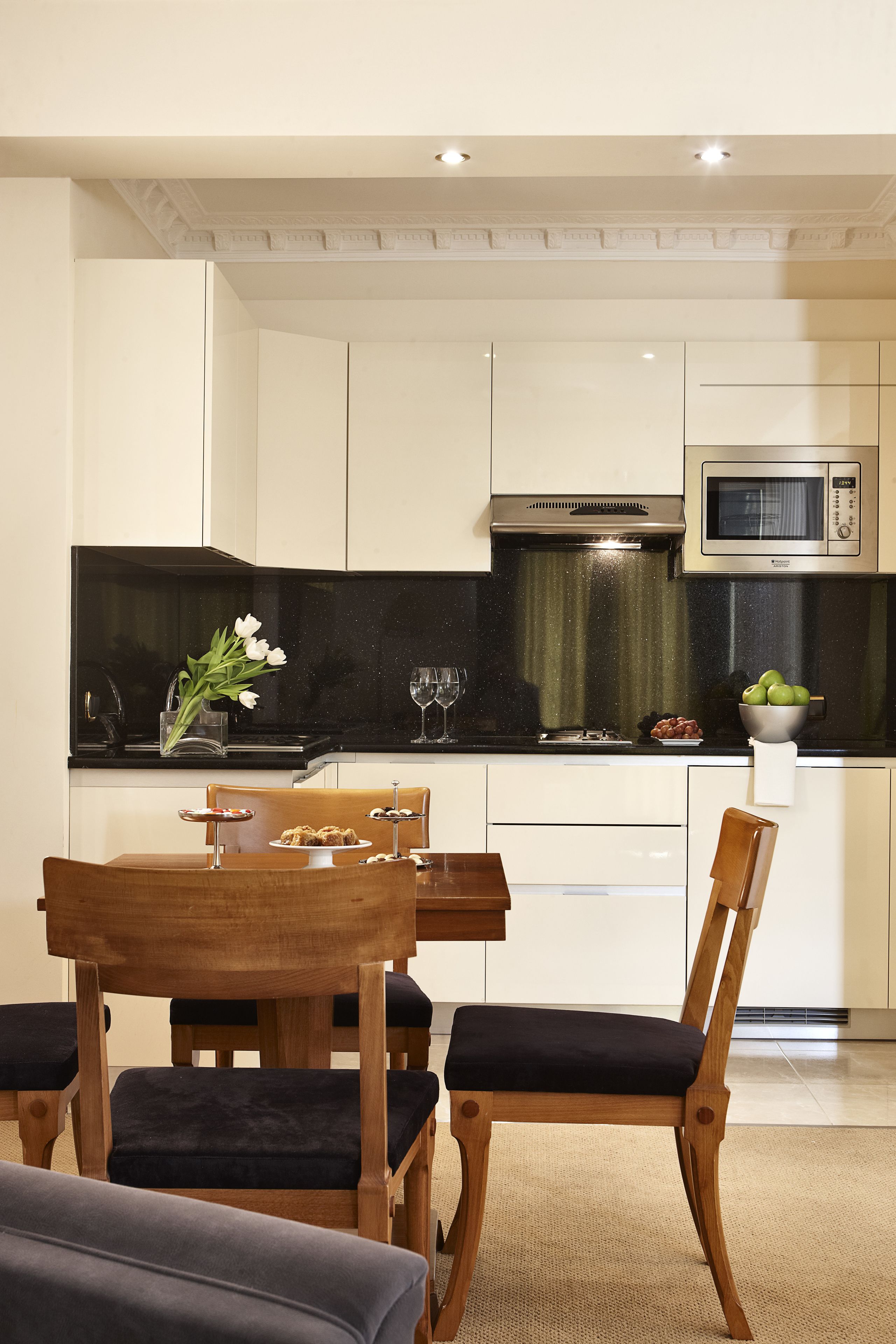 Een moderne keuken met witte kasten, een zwart aanrecht en een houten eettafel met stoelen.