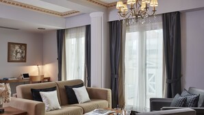 A well-lit hotel room with a beige sofa, a wooden coffee table, and a chandelier.