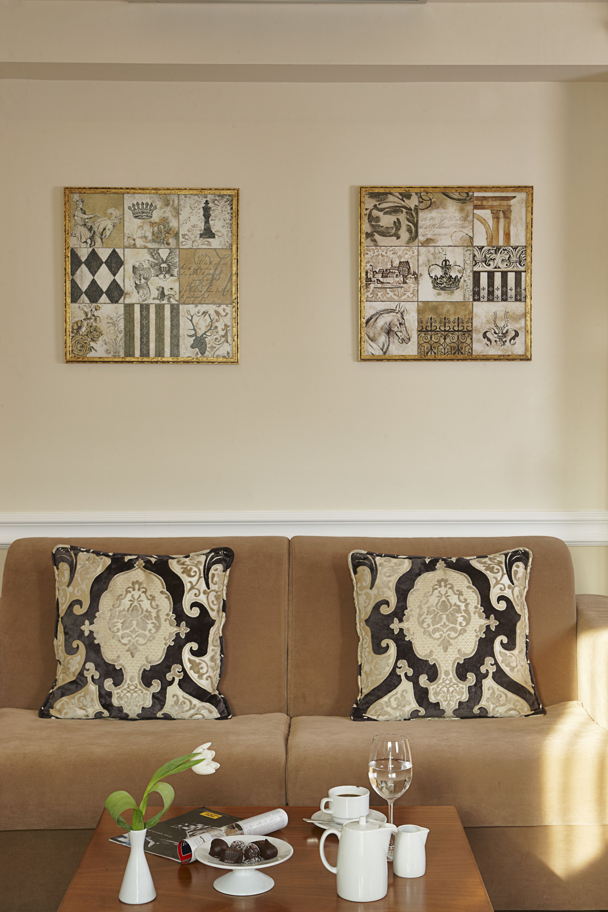 Una sala de estar con un sofá marrón, dos almohadones decorativos, una mesa de centro con un jarrón, un vaso y una jarra.
