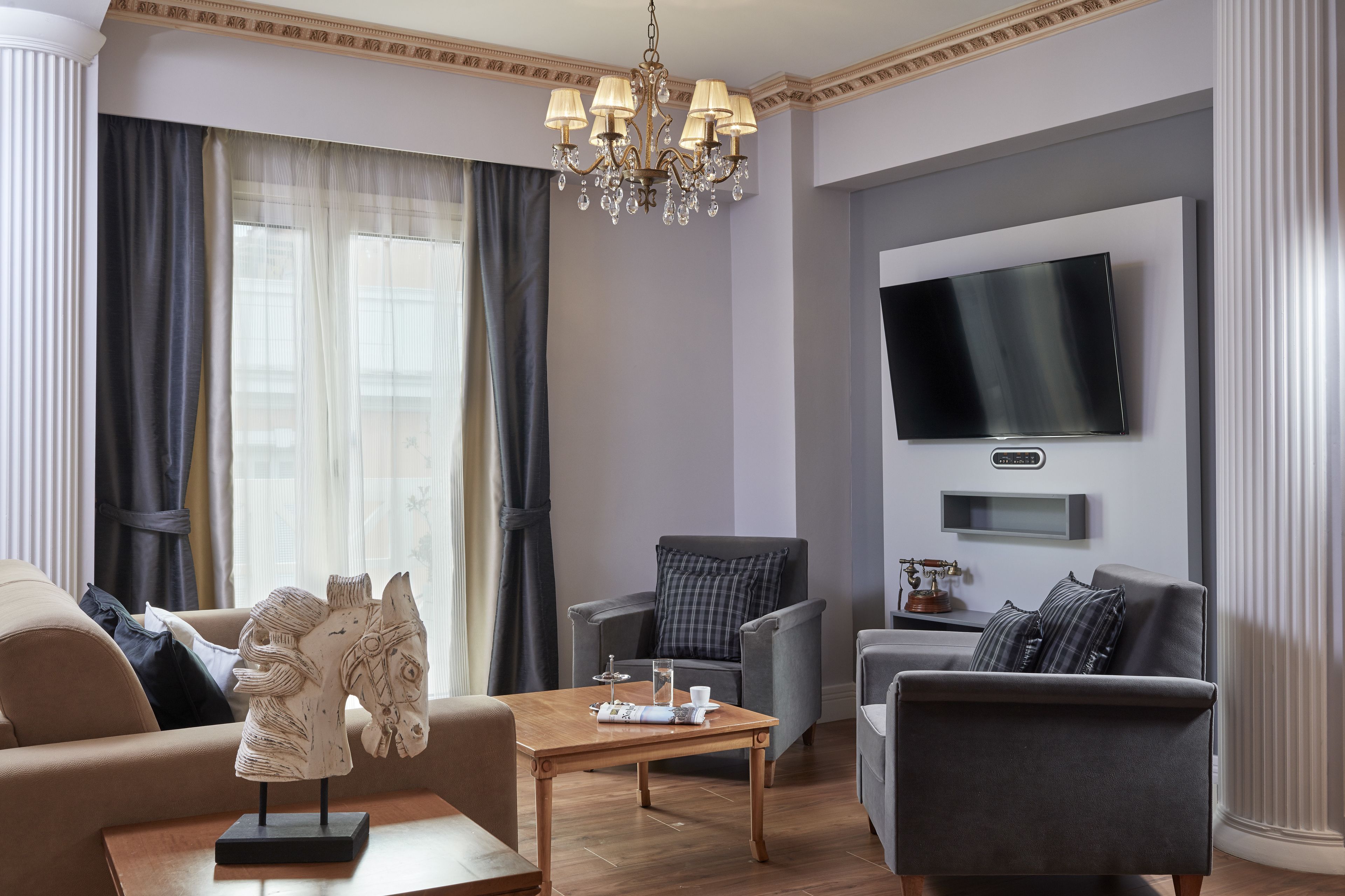 A modern living room with a chandelier, a flat-screen TV, and a horse sculpture on a coffee table.