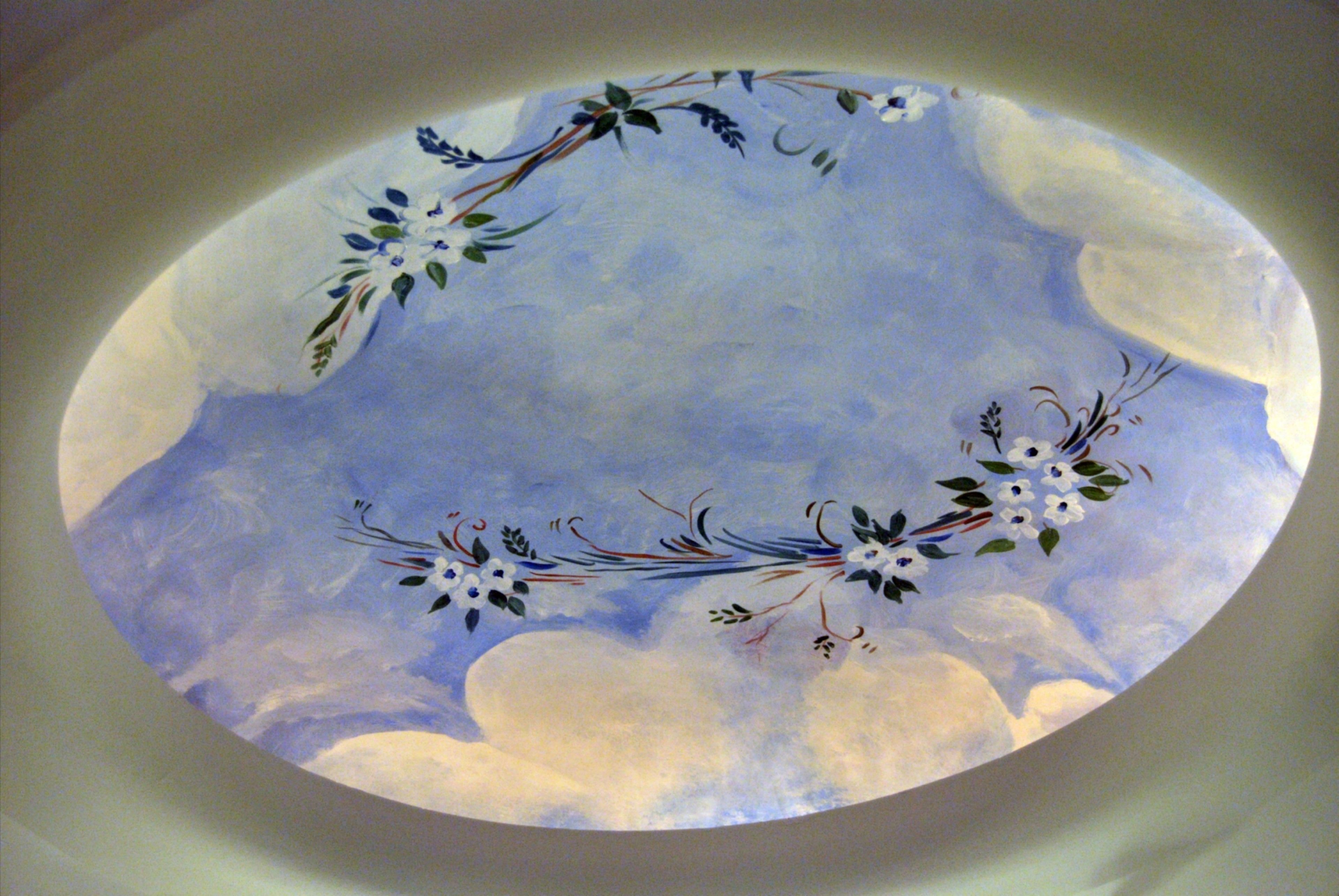 Techo circular con cielo y nubes pintados, adornado con diseños florales y aves.