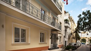 A multi-story building with balconies, a flag, and parked cars along the street.