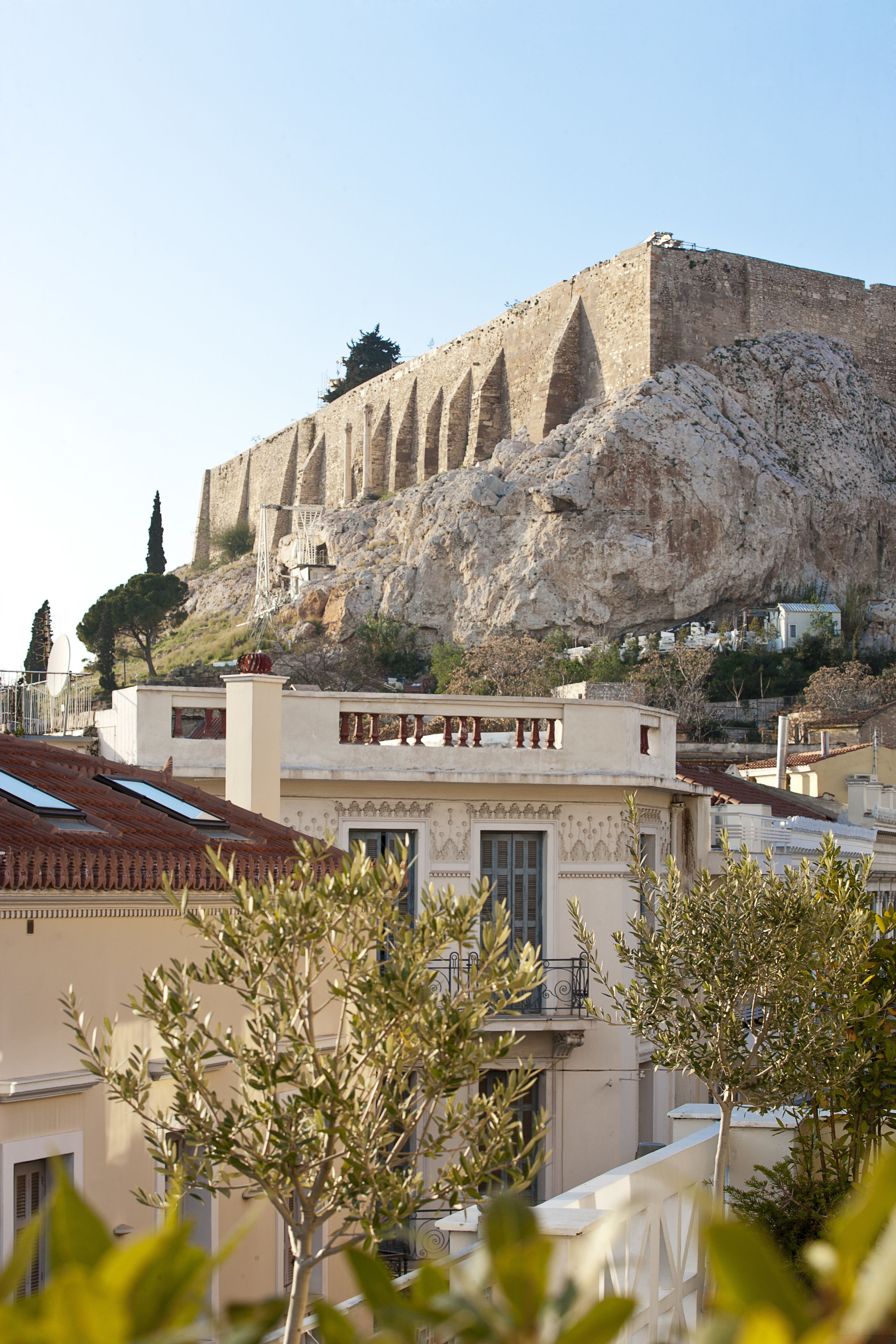 A historic stone fortress with battlements, modern buildings in the foreground, and a clear sky.