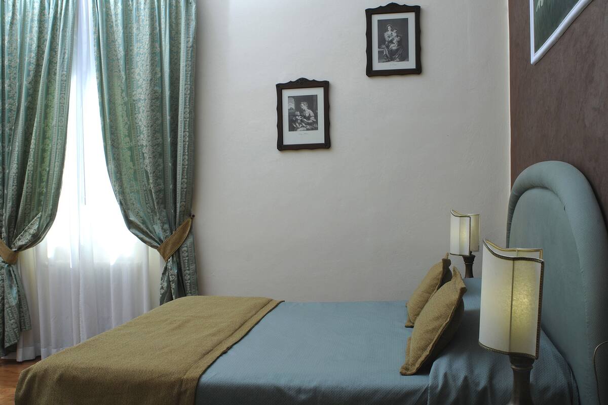 A bedroom with a bed, two framed pictures on the wall, and a nightstand with two lamps.