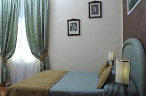 Un dormitorio con una cama, dos cuadros en la pared y una mesita de noche con dos lámparas.