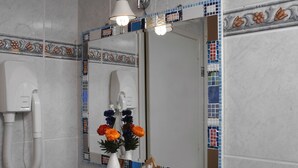 A bathroom with a white telephone, a mirror with mosaic tile borders, and a vase with flowers on the counter. - B&B Dante e Beatrice (Florence)
