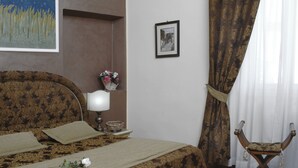 A bedroom with a patterned bedspread, a bedside lamp, a vase with flowers, a framed picture on the wall, and a chair with a curtain. - B&B Dante e Beatrice (Florence)