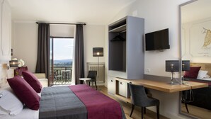 A hotel room with a bed, a desk, a chair, a TV, and a balcony with a view. - La Cisterna (San Gimignano)