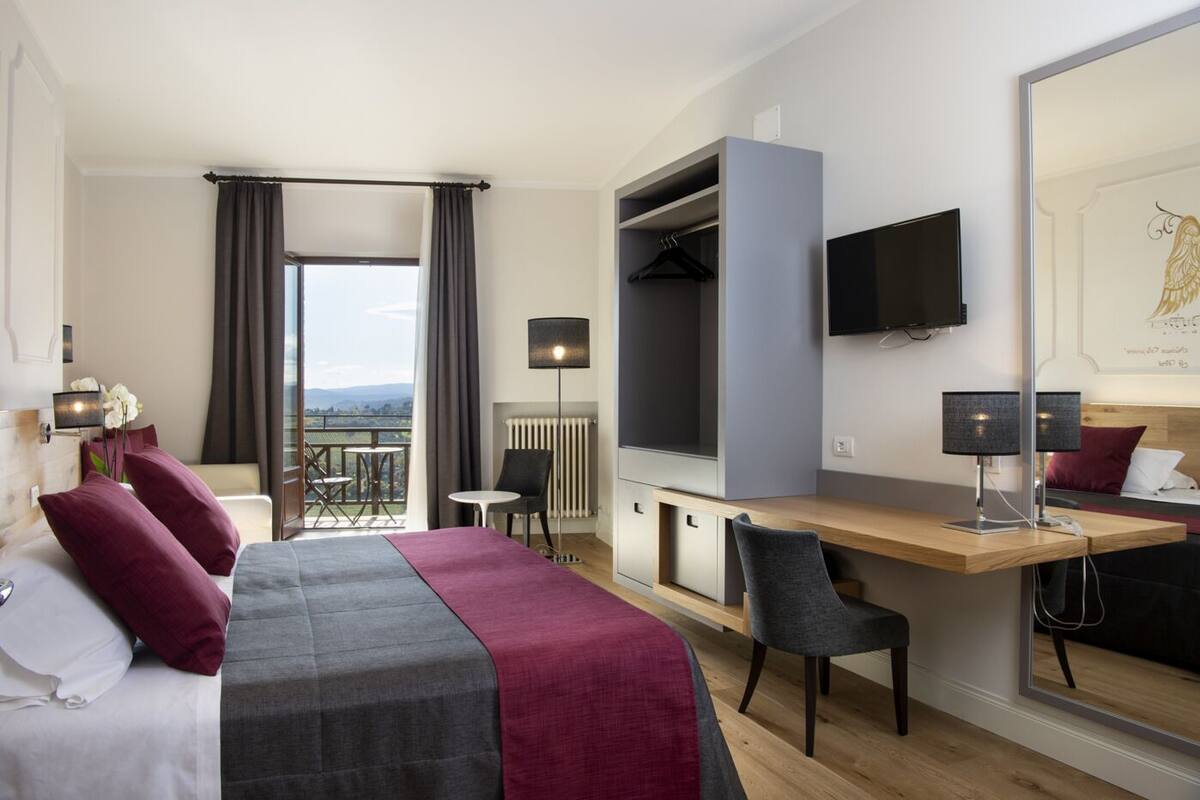A hotel room with a bed, a desk, a chair, a TV, and a balcony with a view.