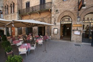 An outdoor cafe with tables and chairs, a brick building with arches, and a sign for 'Albergo Ristorante'. - La Cisterna (San Gimignano)