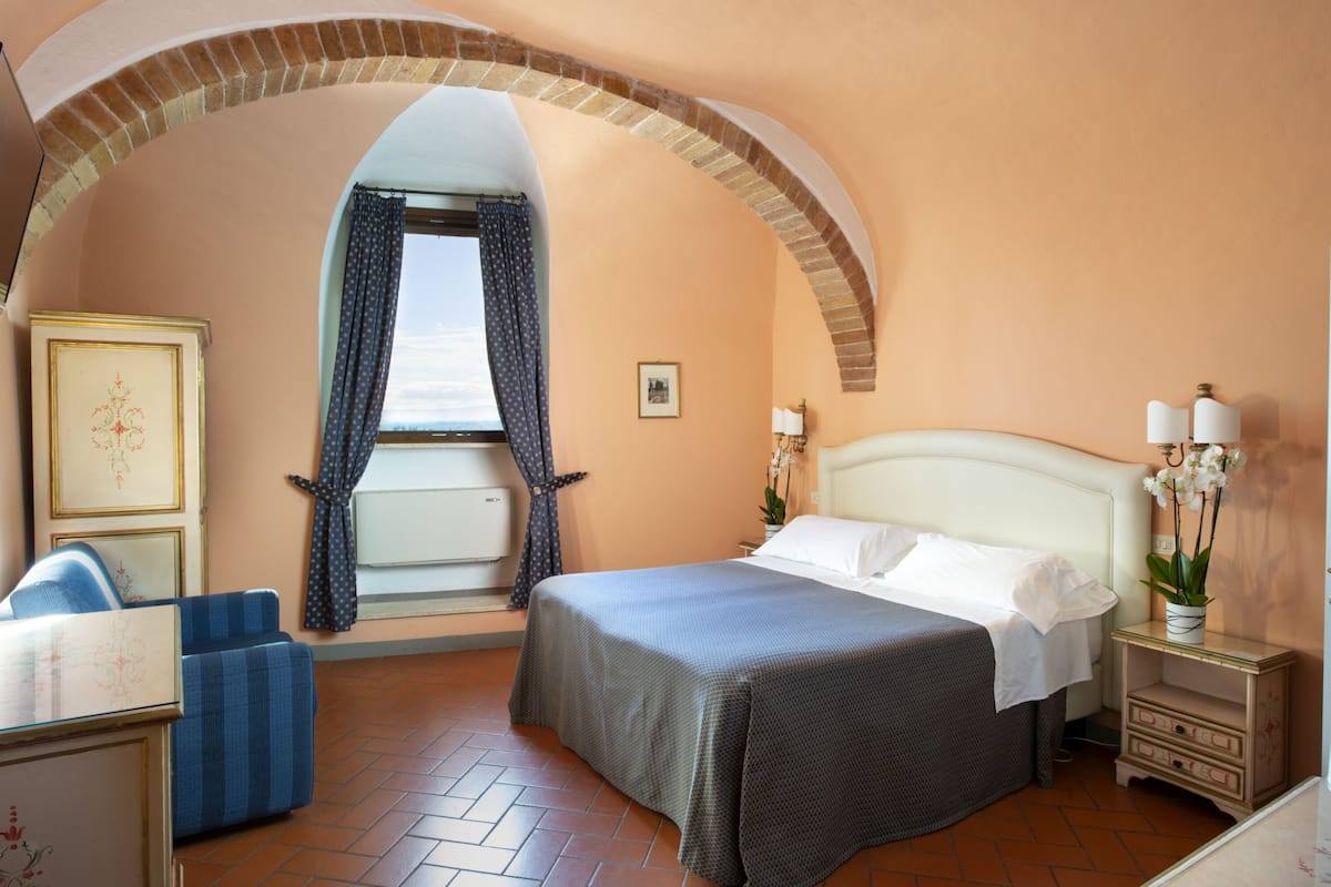 A hotel room with a bed, a chair, a nightstand, and a window with curtains.