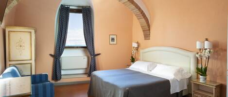 A hotel room with a bed, a chair, a nightstand, and a window with curtains.