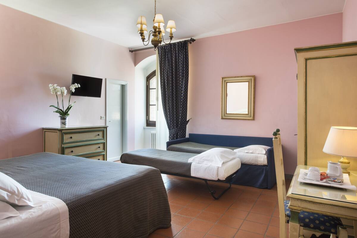 A hotel room with two beds, a TV, a desk with a lamp, and a window with curtains.