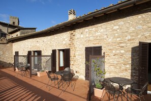 A stone building with outdoor seating and a tiled patio. - La Cisterna (San Gimignano)