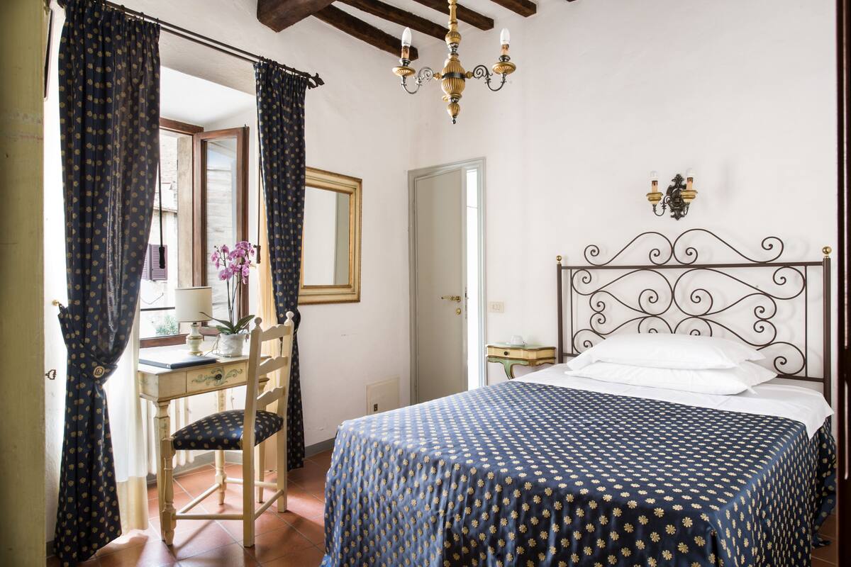 A bedroom with a bed, a desk, a chair, and a chandelier.