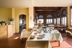 A dining area with multiple tables set for breakfast, featuring a variety of pastries and fruits. - La Cisterna (San Gimignano)