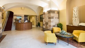A lobby with a reception desk, a staircase, and seating areas. - La Cisterna (San Gimignano)