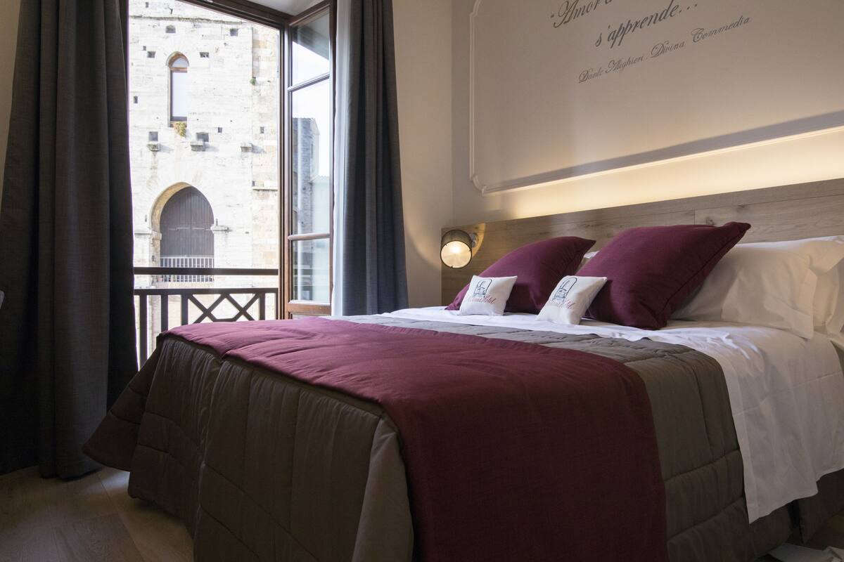 A hotel room with a large bed, a view of a historic building, and a wall with a quote.