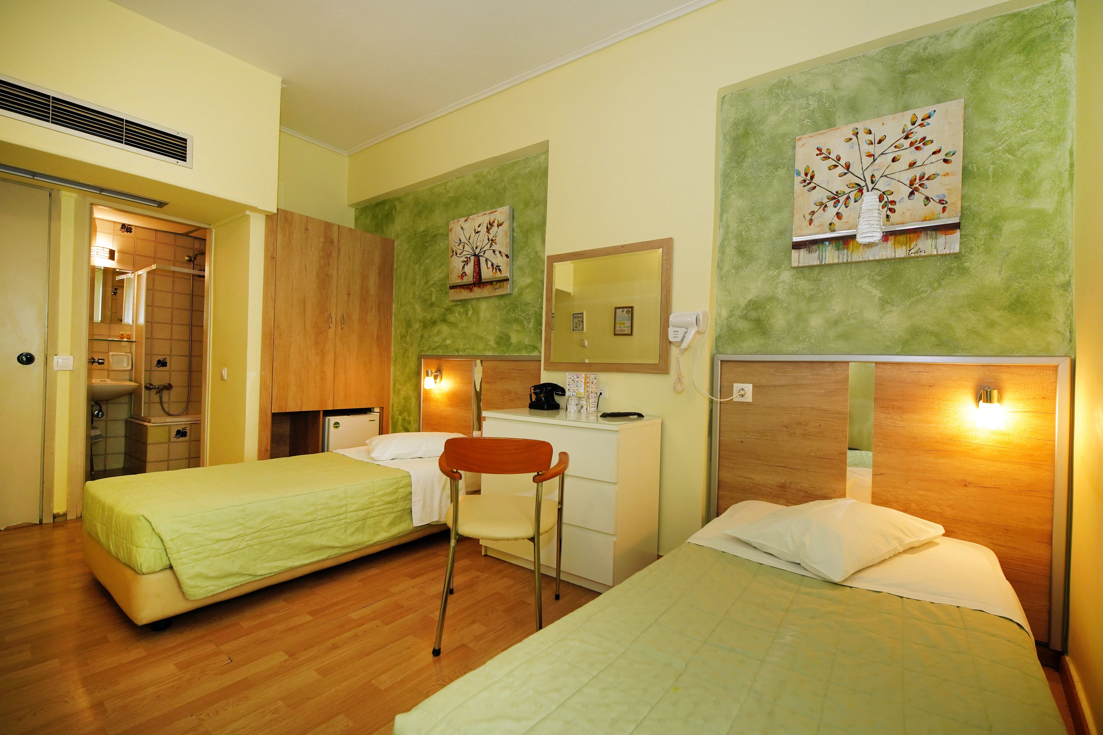 A hotel room with two beds, a desk, a chair, and a shower area.