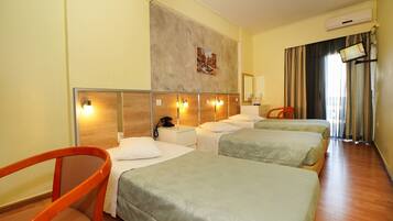 A hotel room with three beds, a wooden headboard, a painting on the wall, a flat-screen TV, and a wooden floor.