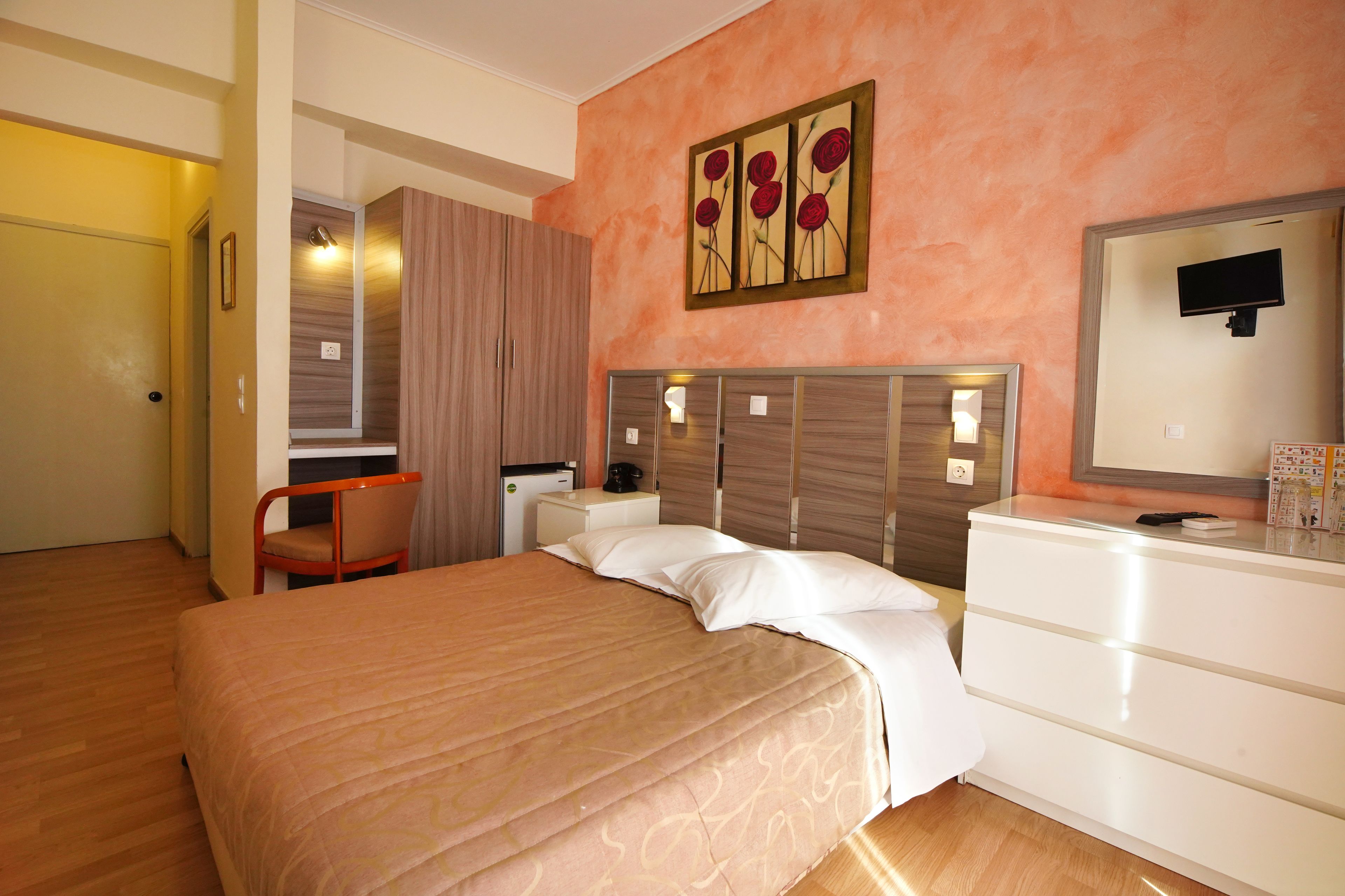 Una habitación de hotel con cama, cómoda, silla, escritorio y un cuadro en la pared.