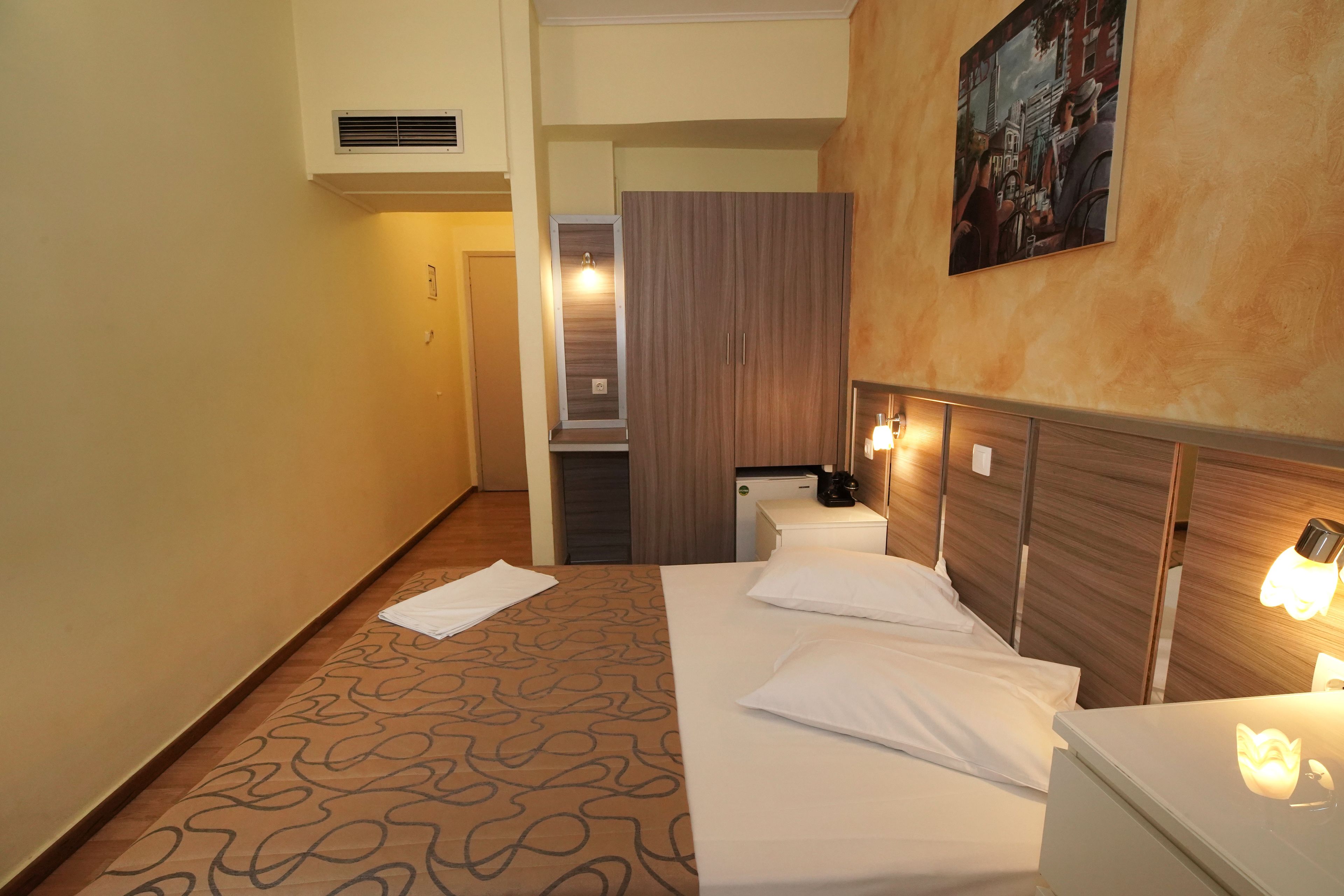 Una habitación de hotel con cama, mesitas de noche, un escritorio pequeño, un cuadro en la pared y una puerta que da a otra habitación.