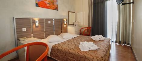 A hotel room with a bed, a desk, a chair, a painting on the wall, and a window with curtains.