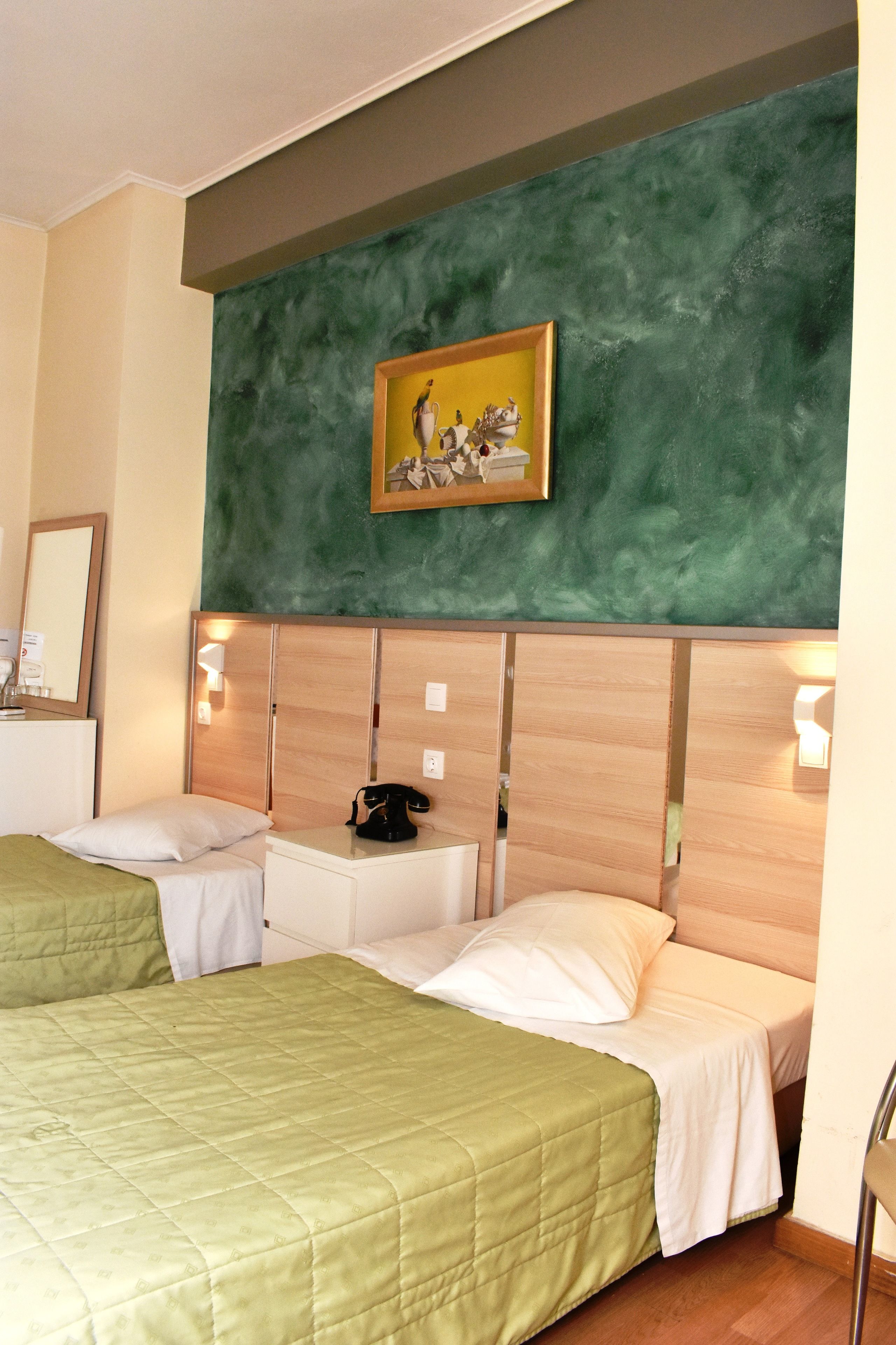 A hotel room with two beds, a green wall, a painting, and a bedside table with a telephone.
