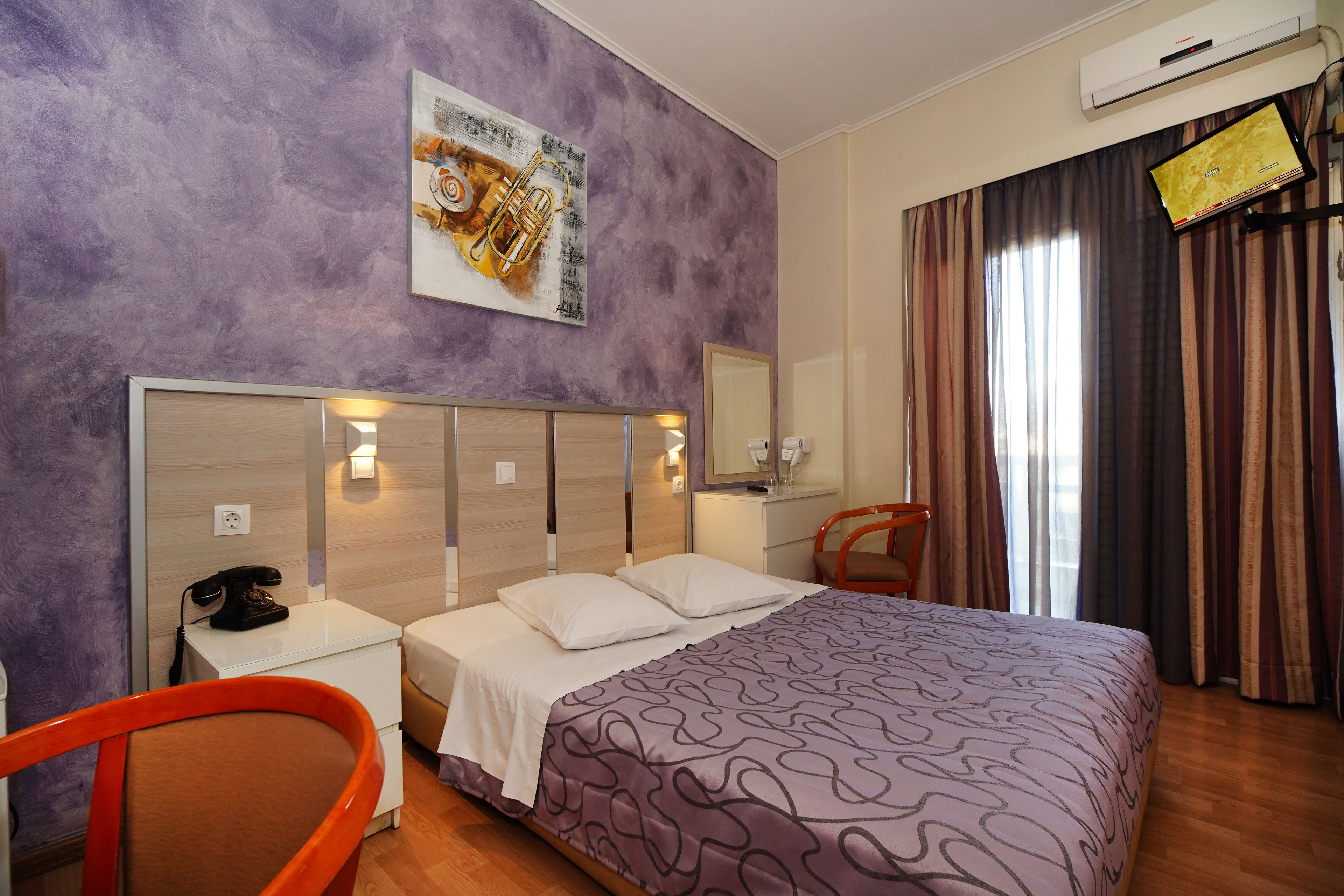 A hotel room with a bed, a nightstand, a chair, a mirror, and a wall-mounted TV.