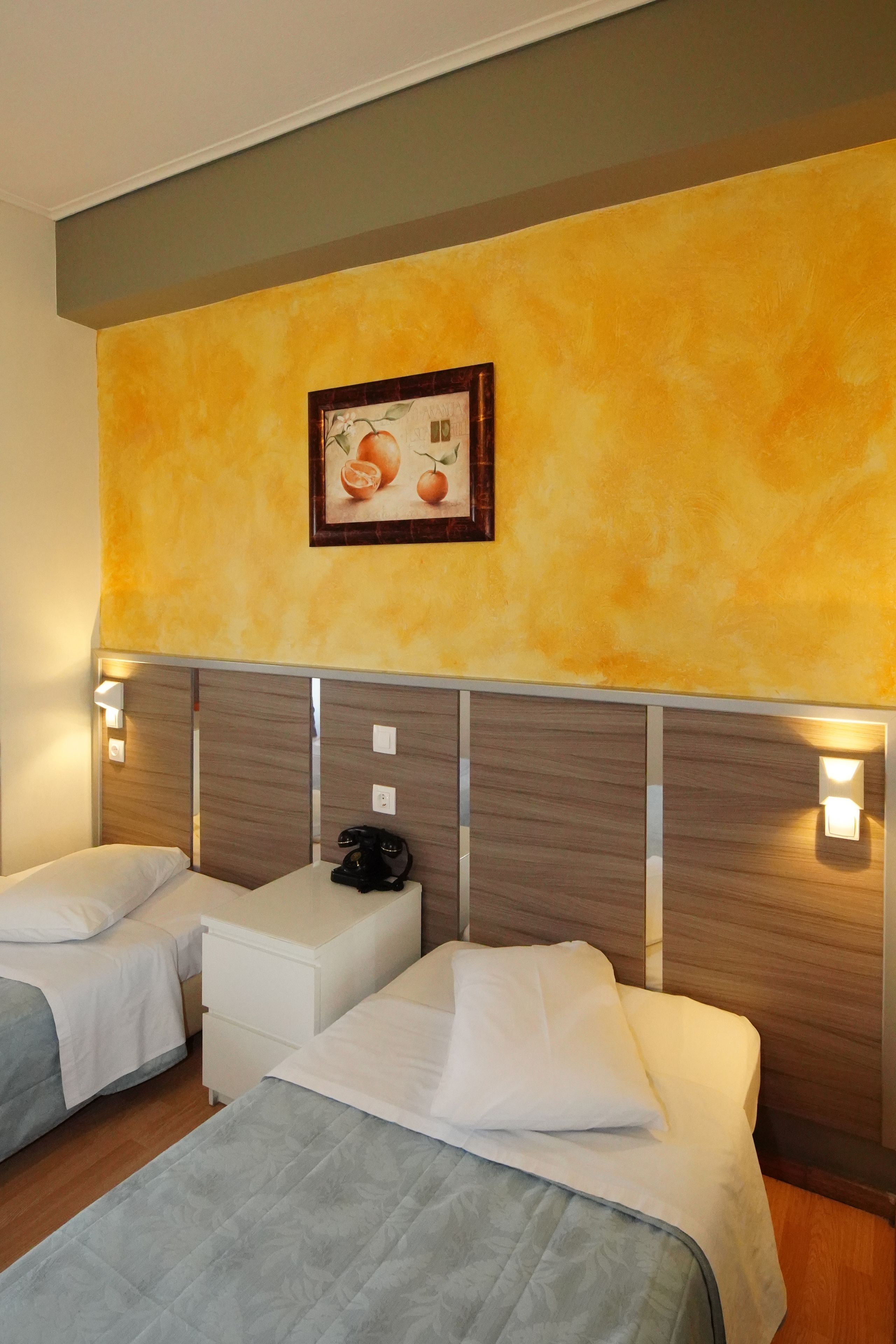 A hotel room with two beds, a small bedside table, a telephone, and a painting on the wall.