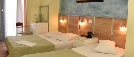 Habitación de hotel con dos camas individuales, un escritorio con teléfono, una silla, un espejo y un cuadro en la pared.