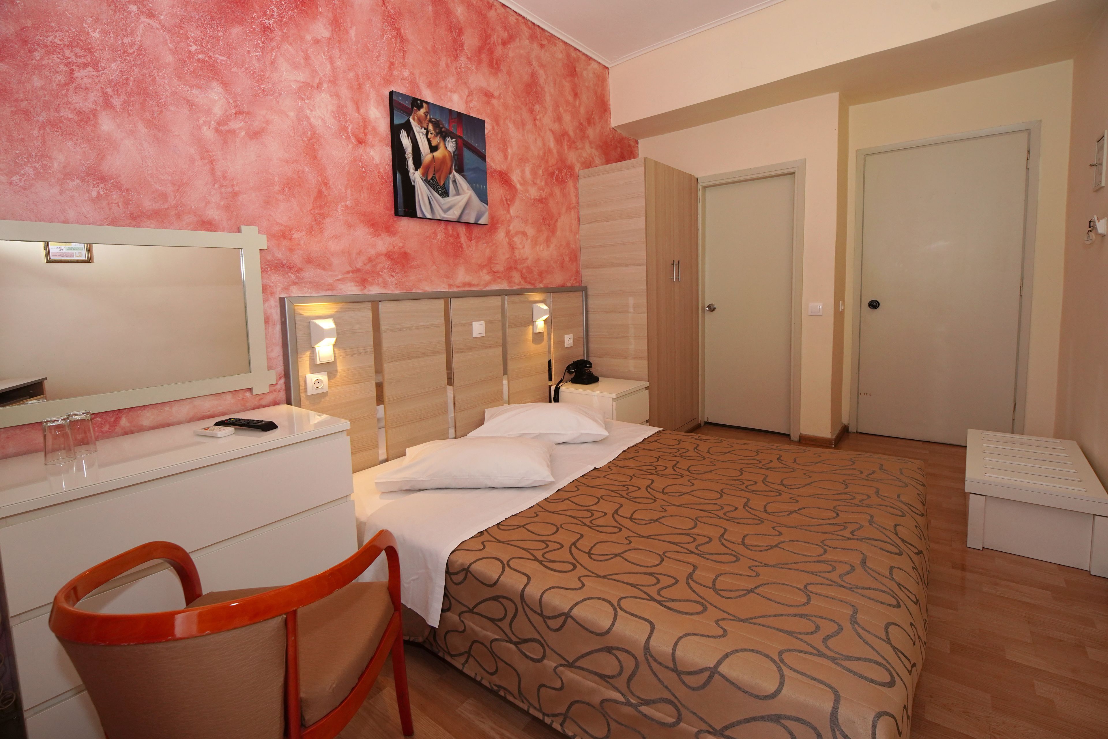 Ein Hotelzimmer mit einem Bett, einem Schreibtisch mit Stuhl, einem Spiegel, einem Nachttisch und einer Tür.