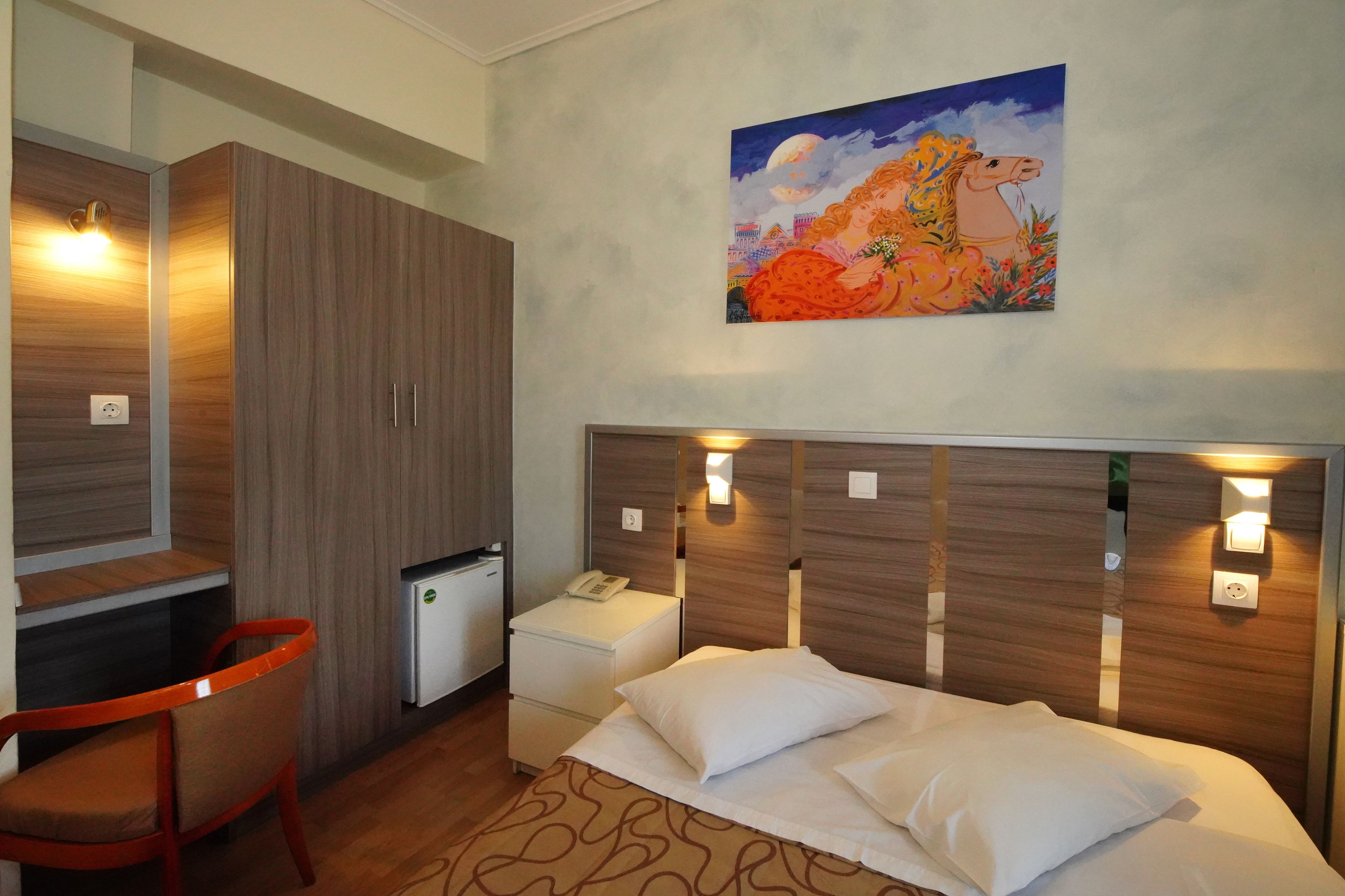 Une chambre d’hôtel équipée d’un lit, d’un bureau, d’une chaise, d’un petit réfrigérateur et d’un tableau au mur.
