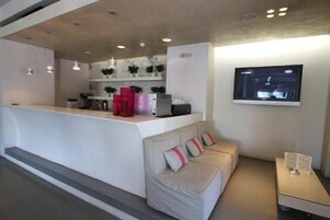 Una hall d'albergo moderna con una reception, un divano e uno schermo televisivo.