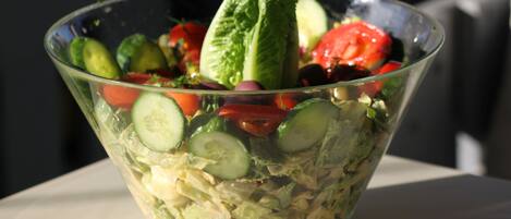 A clear glass bowl containing a salad with lettuce, tomatoes, cucumbers, and olives.