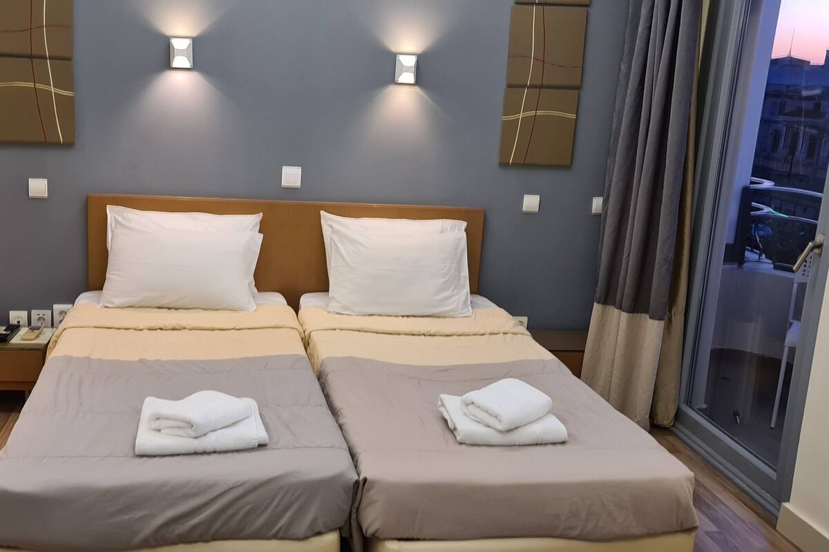Ein Hotelzimmer mit zwei Betten, einem Nachttischtelefon und einem Fenster mit Blick auf die Stadt.