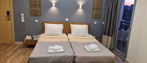 A hotel room with two beds, a bedside telephone, and a window with a view of the cityscape.
